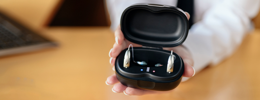 Image of hands holding an open hearing aid charger containing hearing aids